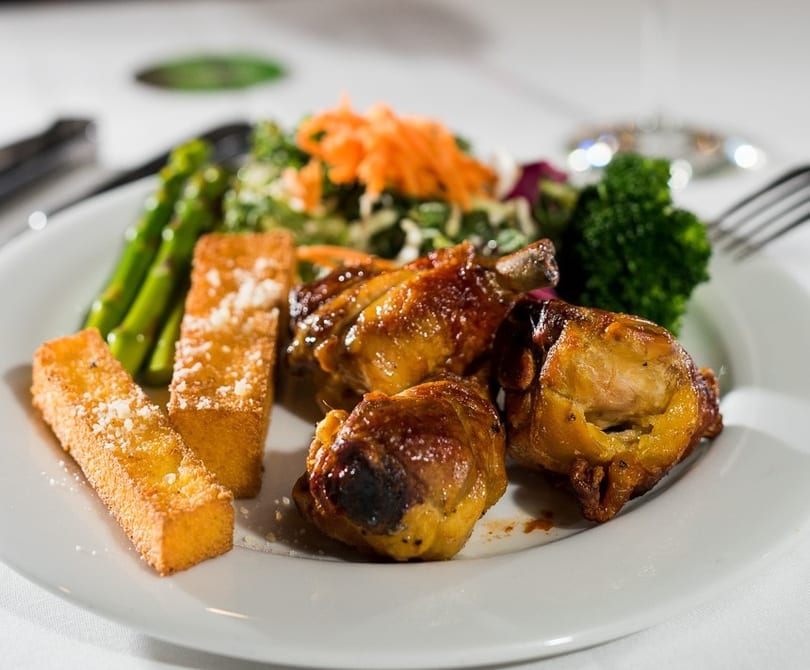 A plate of roasted chicken pieces, asparagus, polenta fries, and a side salad with broccoli.