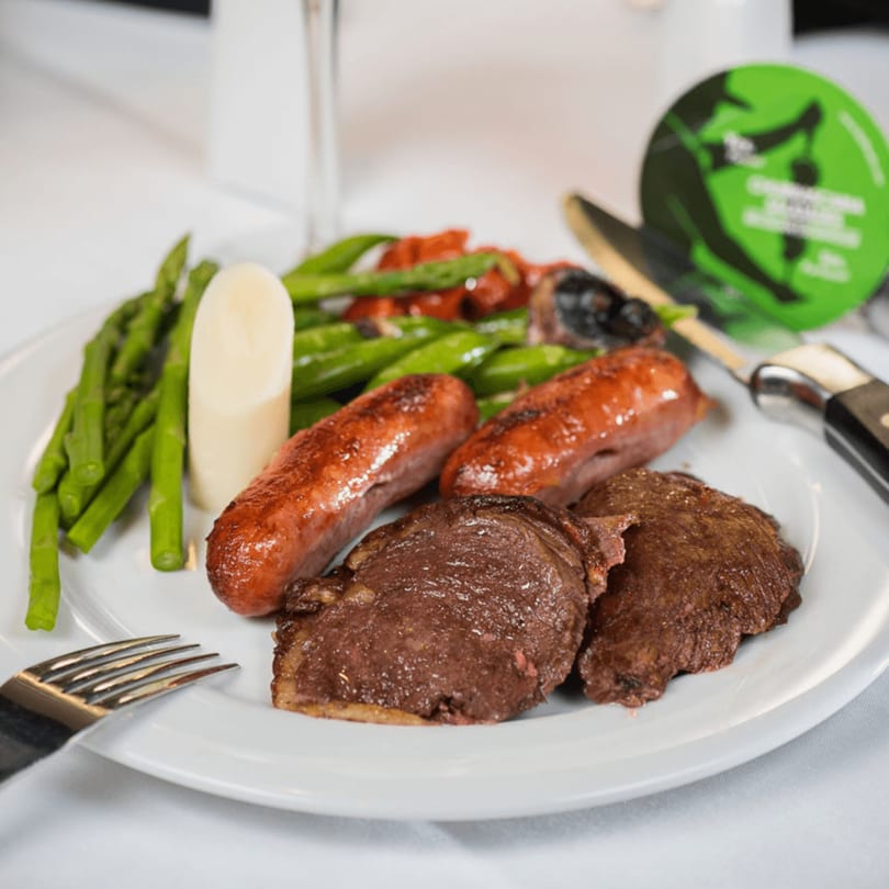A plate of grilled steak, sausages, asparagus, and other vegetables on a white tablecloth.